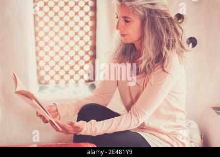 Ritratto di mezza età bella donna caucasica che legge un libro a casa godendo del tempo - persone e rilassarsi a casa - femmina con capelli lunghi grigio studio si Foto Stock