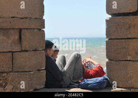 Teenager marocchini, ragazzi che riposano sul muro vicino al mare. Essaouira, Marocco, Africa. Foto Stock