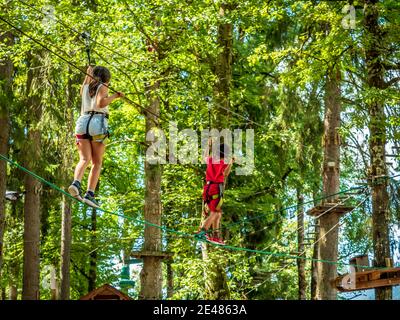 Corso di corde alte a Morillon (Alpi francesi): Bambini tra gli alberi. Due bambini che tentano di camminare ed equilibrarsi su una corda legata tra alberi *** lo Foto Stock