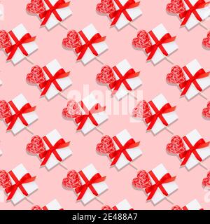 Motivo natalizio senza cuciture per San Valentino con scatola regalo bianca, nastro rosso e lollipop cardiaco su sfondo rosa pastello. Foto Stock