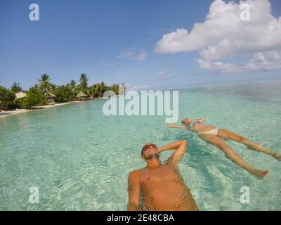 Giovane bella coppia che giace e galleggia sul retro in acque turchesi di mare sulla spiaggia paradiso tropicale a Bora Bora Island, Polinesia Francese. Foto Stock