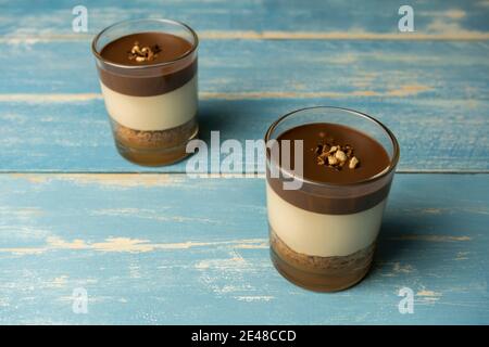 Due dessert al cioccolato in vetro (yogurt o crema, biscotti e noci) concetto dolce caramelle su sfondo di legno estivo blu. Foto Stock