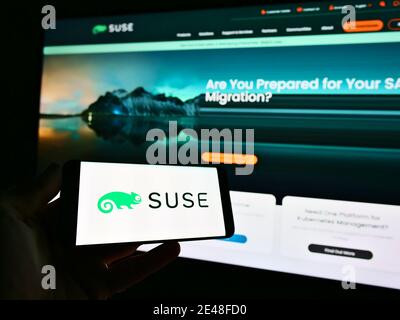 Persona in possesso di smartphone con il logo dello sviluppatore di software tedesco SUSE Software Solutions Germany GmbH in esposizione. Mettere a fuoco sulla sinistra dello schermo del telefono. Foto Stock