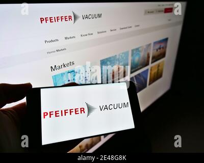 Persona che tiene lo smartphone con il logo del produttore tedesco di pompe Pfeiffer Vacuum Technology AG su schermo con il sito web. Mettere a fuoco lo schermo del telefono cellulare. Foto Stock