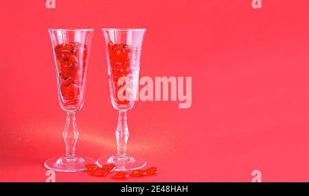 Due bicchieri di champagne sono riempiti di cuori di vetro su uno sfondo rosso con spazio per il testo. San Valentino, amore, appuntamento romantico Foto Stock