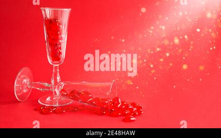 Due bicchieri di champagne sono riempiti di cuori di vetro su uno sfondo rosso con spazio per il testo. San Valentino, amore, appuntamento romantico Foto Stock
