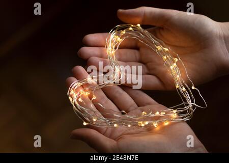 Le mani di una giovane ragazza tengono un cuore fatto di luci LED. Immagine romantica non filtrata, piena d'amore per San Valentino. Foto Stock