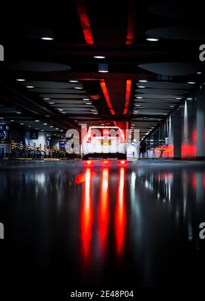 Birmingham Grand Central 14 Giugno 2020 White taxi auto pubblico trasporto in attesa di passeggeri pioggia su strada inondata luci riflettenti freno luci scure Foto Stock