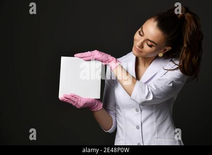 Giovane sorridente bella donna terapeuta medico in uniforme bianca e. guanti di protezione in lattice per fogli di carta bianchi Foto Stock