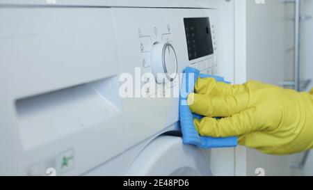 Le mani dell'uomo indossano i guanti protettivi bianchi per uso domestico pulisce e disinfettano La lavatrice Foto Stock