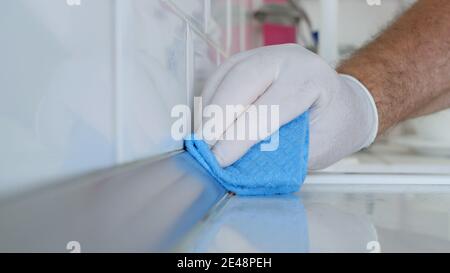 Uomo con Guanti domestici bianchi di protezione in mani, pulisce e disinfetta i mobili da cucina Foto Stock