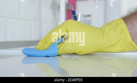 Uomo con Guanti domestici bianchi di protezione in mani, pulisce e disinfetta i mobili da cucina Foto Stock