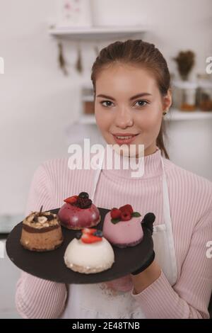 Immagine verticale di una giovane donna di charme che tiene un piatto con dessert al suo caffè Foto Stock