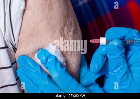 L'uomo molto anziano sta ricevendo il vaccino del coronavirus. Primo piano. Iniezione a persone anziane a casa. Siringa con medici mani in guanti blu. Foto Stock