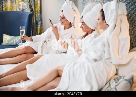 Tre belle donne che si rilassano e scorrono sul telefono a letto Foto Stock