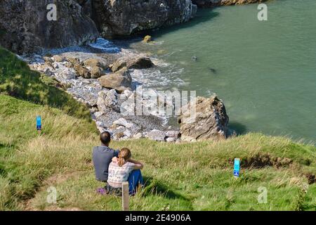 Una coppia sulla scogliera guarda un paio di foche grigie nelle fiasche di Angel Bay alla fine del Little Orme, Galles del Nord Foto Stock