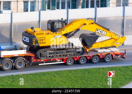 Escavatore rimorchio JCB camion caricato sul trasporto di carico su una piattaforma rimorchio autostrada urbana. Russia, San Pietroburgo. 07 maggio 2020 Foto Stock