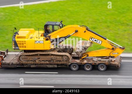 Rimorchio per autocarri JCB dell'escavatore caricato sulla piattaforma di carico sull'autostrada urbana. Russia, San Pietroburgo. 18 maggio 2020 Foto Stock