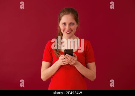 Bionda ragazza sorridente con il telefono in mani su sfondo rosso Foto Stock