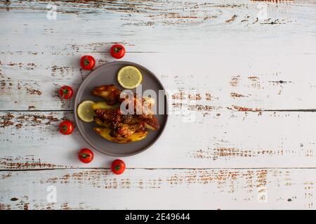 Ali di pollo con miele e spicchi di patate su un piatto con pomodori ciliegini Foto Stock