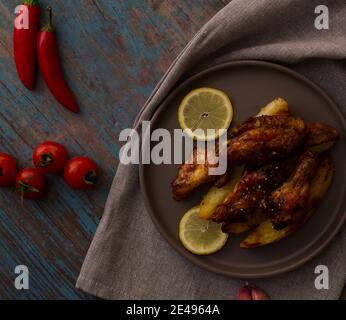 Ali di pollo con miele e spicchi di patate su un piatto con pomodori ciliegini e peperoncini Foto Stock