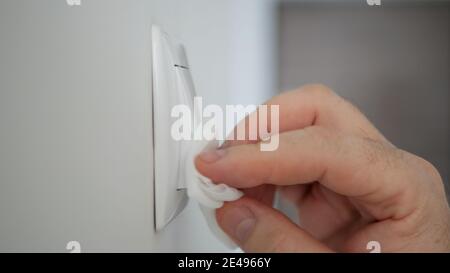 Uomo pulizia e disinfezione interruttore luce dalla sala ufficio Utilizzo di disinfettanti contro i virus Covid-19 Foto Stock