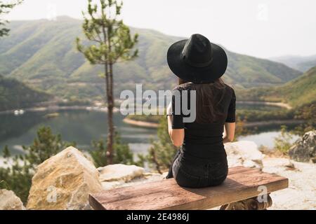 La giovane donna è seduta sulla panchina e guardando stupefacente natura Foto Stock