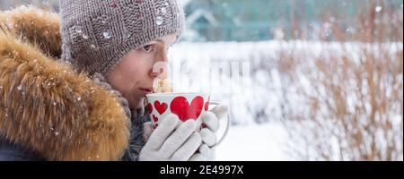 donna di mezza età che tiene una tazza di bevanda calda e sorridente sullo sfondo di una strada invernale. sparare all'aperto. Foto Stock