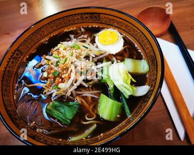 Ciotola di zuppa di Ramem di Japanes con cucchiaio di legno e bastoncini di pollo. Foto Stock