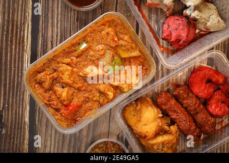 Vista dall'alto della cucina tradizionale indiana in una scatola di plastica su un tavolo di legno. Consegna di fast food indiano a casa. Foto Stock