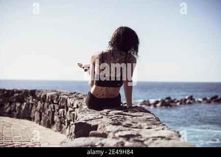 fit donna con albero tatuaggio siede dal bordo dell'oceano con il cane carino sul giro Foto Stock