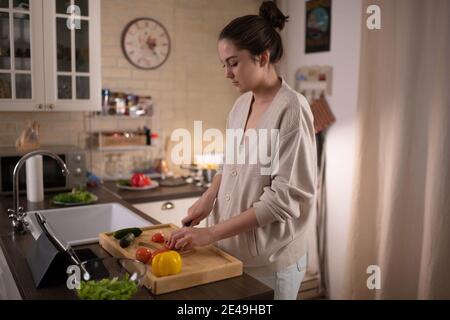 Giovane donna tritare le verdure per l'insalata mentre si guarda corso di cucina su tablet Foto Stock