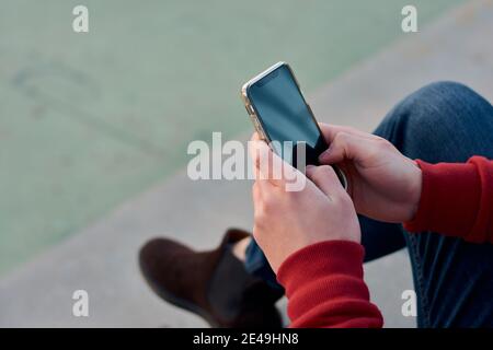 L'uomo studentesco irriconoscibile usa il suo telefono in un campo da basket Foto Stock