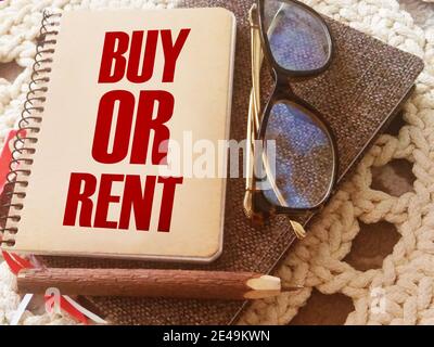 La domanda per comprare o affittare ha digitato su una copertina di libro, occhiali e penna. Analisi del mercato immobiliare e delle finanze personali. Concetto aziendale. Foto Stock