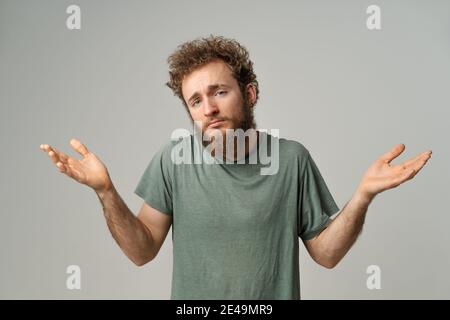 Bell'uomo con capelli ricci che mostra che non conosco il gesto con entrambe le mani isolate su sfondo bianco. Ritratto di giovane confuso su bianco Foto Stock