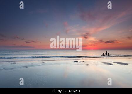 Persone che nuotano nel Mare del Nord poco dopo il tramonto sulla spiaggia sull'isola di Romo, Danimarca Foto Stock