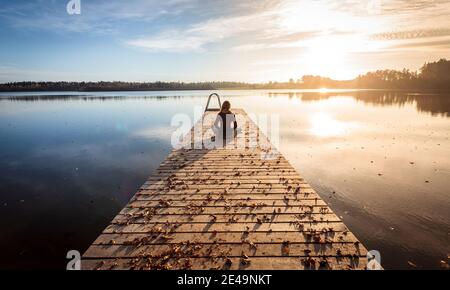 Giovane donna seduto, rilassante e facendo yoga sul molo o molo al lago, mentre il tramonto Foto Stock