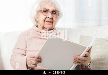 Donna anziana che guarda le foto in album fotografico bianco Foto Stock