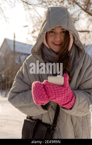 Donna con frettole in abiti invernali con mittens per uso all'aperto il suo smartphone Foto Stock