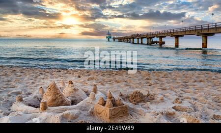 Molo e spiaggia con castelli di sabbia in primo piano a Zinnowitz al tramonto. Mar Baltico, isola Usedom, Germania Foto Stock