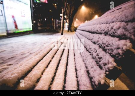 panca di legno nella strada di una città coperta da neve che è caduta in inverno Foto Stock