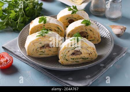 Rotolo di lavasch con spratti, formaggio cremoso, cetriolo e uova su un piatto grigio su sfondo azzurro. Foto Stock