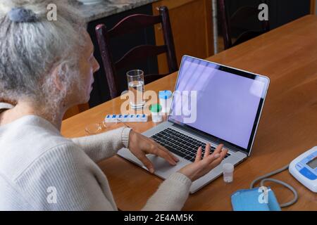 Donna caucasica anziana che ha videochiamata consultazione medica utilizzando il laptop in cucina Foto Stock