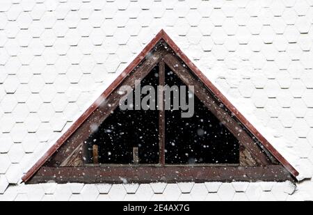 Il dormitorio senza vetro nelle finestre sul tetto nevoso. Caduta di neve sul tetto della casa con una finestra senza vetro. Foto Stock