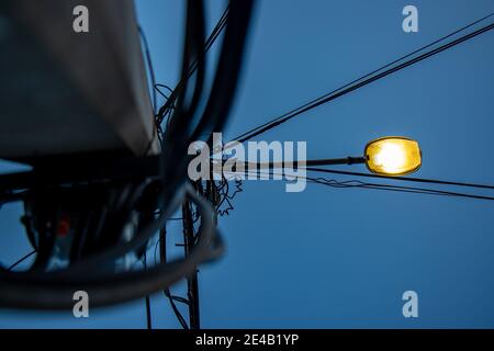 Lampada stradale che brilla contro il cielo blu scuro. Palo di linee elettriche con lampada brillante sulla strada. Foto Stock