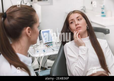 Giovane donna attraente che ha mal di denti, dentista in visita Foto Stock