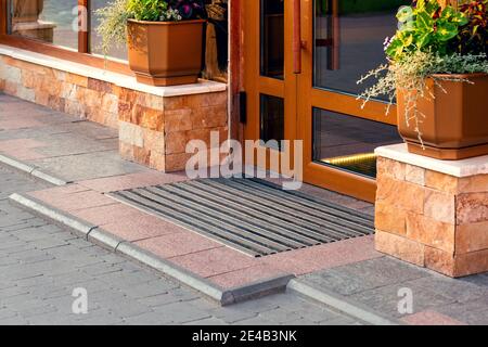 soglia con un tappetino alla porta d'ingresso con una facciata in pietra e vasi di fiori, architettura closeup. Foto Stock