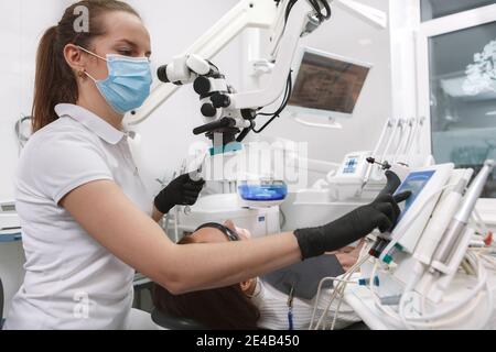 Inquadratura ad angolo ridotto di un dentista professionista che indossa una maschera medica e guanti, utilizzando un moderno microscopio automatico dentistico sul paziente Foto Stock