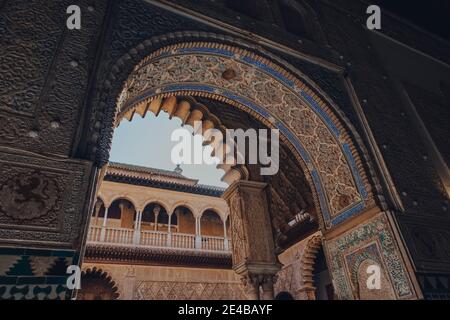 Siviglia, Spagna - 19 gennaio 2020: Vista ad angolo basso di archi ornati che conducono al cortile patio de Maidens all'interno dell'Alcazar di Siviglia, un palazzo reale bui Foto Stock