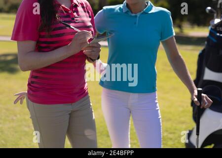 Sezione centrale di due donne caucasiche che giocano il golf una che si riempie fuori scheda di valutazione Foto Stock